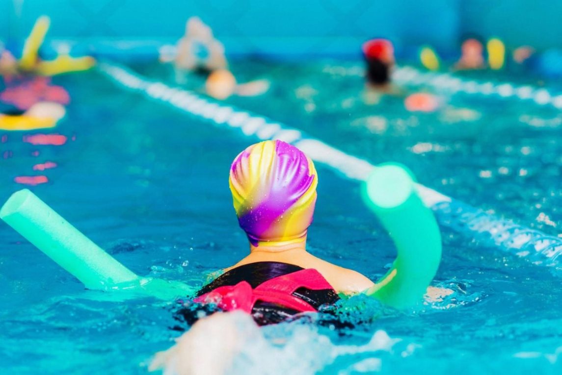 School-aged swimmer with a pool noodle practising in a lane during a group swimming lesson