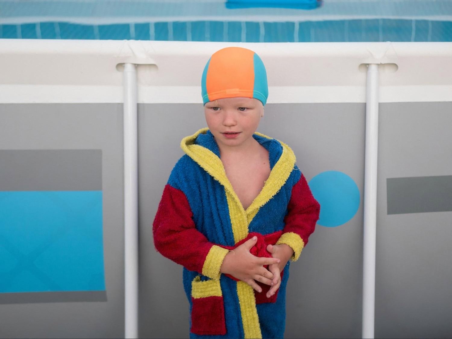 Young child in a colourful robe and swim cap standing next to a school pool after a lesson